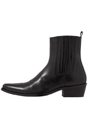 Black leather ankle boots with a pointed toe, vertical stitching accents, and a low block heel, featuring a smooth and polished texture.