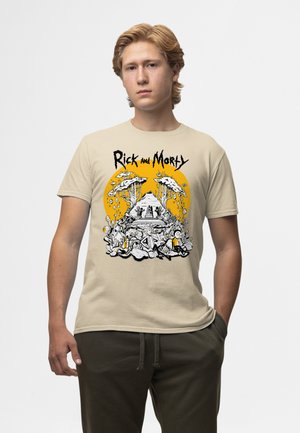 Jonge man met lichtbruin haar die een beige Rick and Morty T-shirt draagt met een afbeelding van een piramide en bomen op een gele achtergrond.