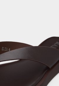 Sandale à enfiler en cuir marron avec une large bride sur le dessus du pied et une semelle plate, présentée sur un fond blanc.