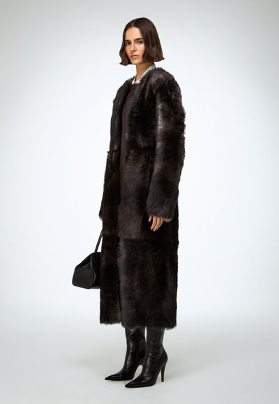 Manteau en fausse fourrure noire au design long et fluide ; texture lisse, large col et manches longues. Associé à des bottes noires à talons aiguilles montant jusqu'aux genoux.