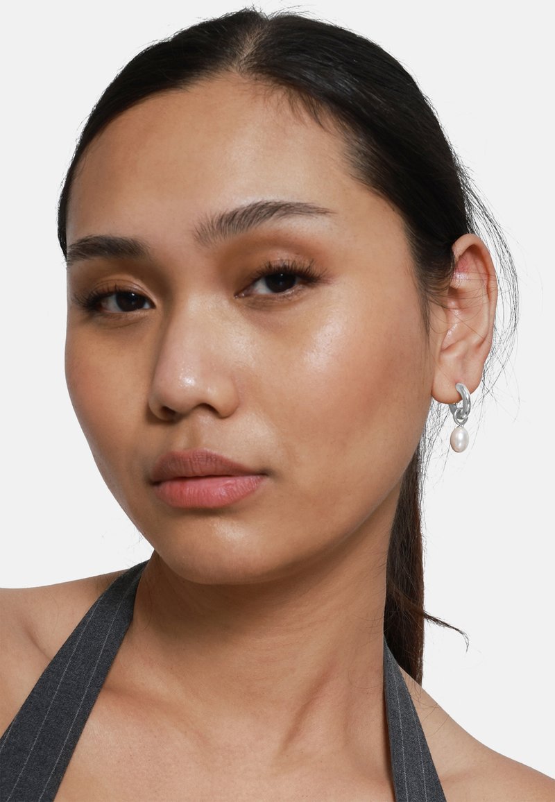 Orecchini a cerchio in argento con pendente a perla. Il modello ha i capelli scuri e indossa un top grigio a righe, mettendo in evidenza gli orecchini.