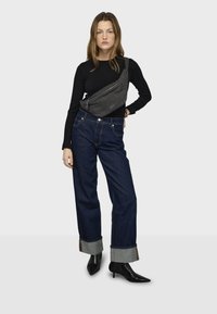 Čierne tričko s dlhým rukávom, tmavé džínsy s širokými nohavicami s vyhrnutými manžetami a sivá kabelka cez rameno. Modelka má na nohách čierne topánky so špičatou špičkou.