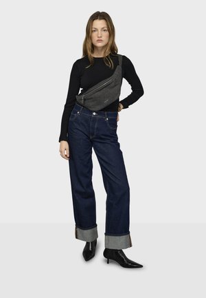 Top negro de manga larga, jeans de mezclilla oscura de pierna ancha con dobladillos doblados y un bolso gris cruzado. La modelo lleva tacones negros de punta puntiaguda.