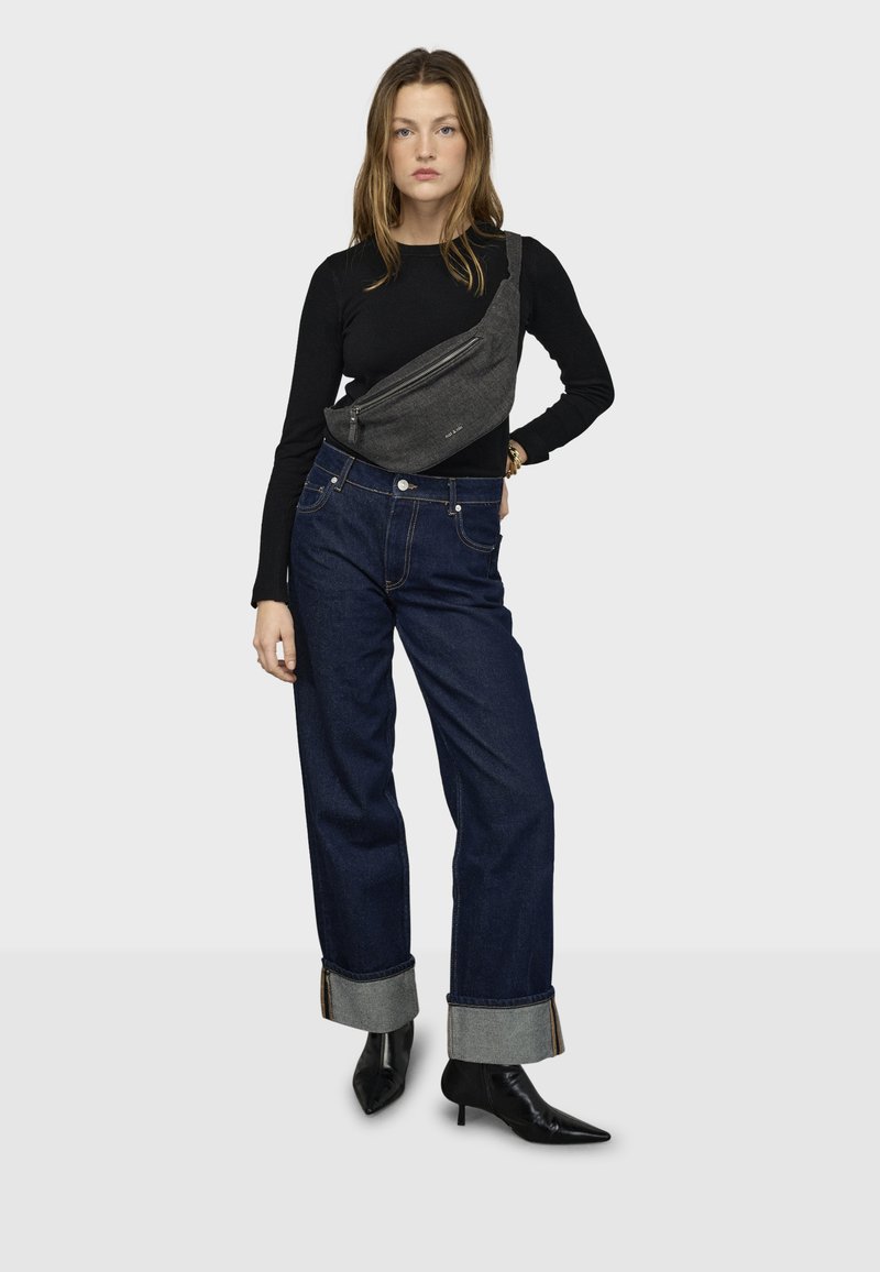 Čierne tričko s dlhým rukávom, tmavé džínsy s širokými nohavicami s vyhrnutými manžetami a sivá kabelka cez rameno. Modelka má na nohách čierne topánky so špičatou špičkou.