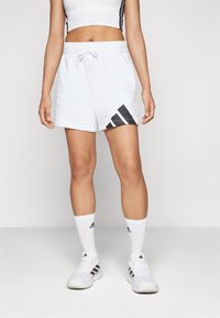 Baltas sporta šortus ar melnu Adidas logotipu un ģeometrisku rakstu, elastīga josta un auklas detaļa. Gluda auduma tekstūra.