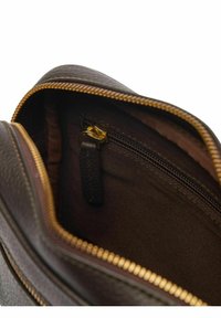 Ruskea nahkalaukun sisäosa, jossa on vetoketjullinen tasku, jossa on kultaisenvärinen vetoketju ja tummasta kankaasta valmistettu vuori, joka esittelee teksturoitua materiaalia.