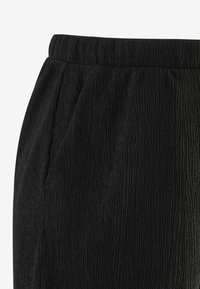 Pantaloni neri con texture e un aspetto stropicciato, dotati di una cintura in vita e tasche laterali. Il tessuto presenta un sottile effetto ondulato.