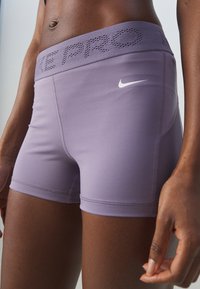 Gros plan sur une personne portant un short de compression Nike Pro violet clair avec une ceinture perforée et le logo swoosh blanc sur la cuisse.