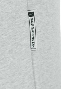 Tejido de sudadera gris con un acabado texturizado. Presenta una etiqueta negra que dice "NIKE STANDARD ISSUE" y un pequeño logo de Nike.
