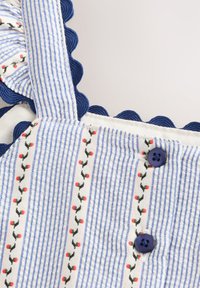 Tissu rayé bleu et blanc avec petite broderie florale rouge, bord festonné bleu foncé et deux boutons bleu foncé sur un vêtement.