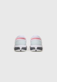 White athletic shoes with a smooth upper, pink accents, and a textured black outsole. Features a cushioned heel and bold branding on the back.