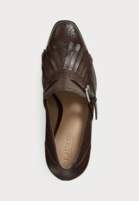 Brown leather shoe with perforated detailing, fringed accents, and a buckle on the side; pointed toe and smooth inner lining.