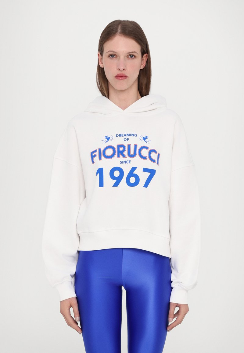 Hvit hettegenser med blå grafikktekst "DRØMMER OM FIORUCCI Siden 1967." Har en avslappet passform og justerbar hette, kombinert med skinnende blå leggings.