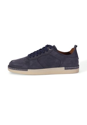 Donkerblauwe suède lage sneaker met dikke donkerblauwe veters, beige rubberen zool en bruine voering, van opzij zichtbaar tegen een witte achtergrond.