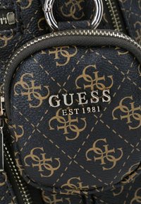 Czarna, teksturowana torba z faux skóry z złotym wzorem i srebrnym logo. Posiada zaokrągloną kieszeń na zamek, przymocowaną za pomocą pierścienia.