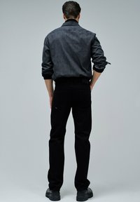 Jeans de mezclilla negra y una camisa de botones gris oscuro, ambos con un diseño ajustado. La camisa tiene las mangas remangadas y un detalle de costura mínimo.