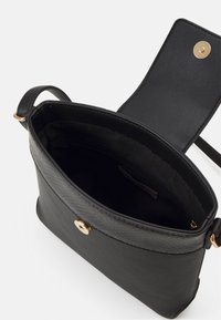 Borsa a tracolla in pelle nera con una trama testurizzata e hardware dorato. Ha una sola tracolla e un'apertura superiore con chiusura a bottone. L'interno è foderato in tessuto nero.