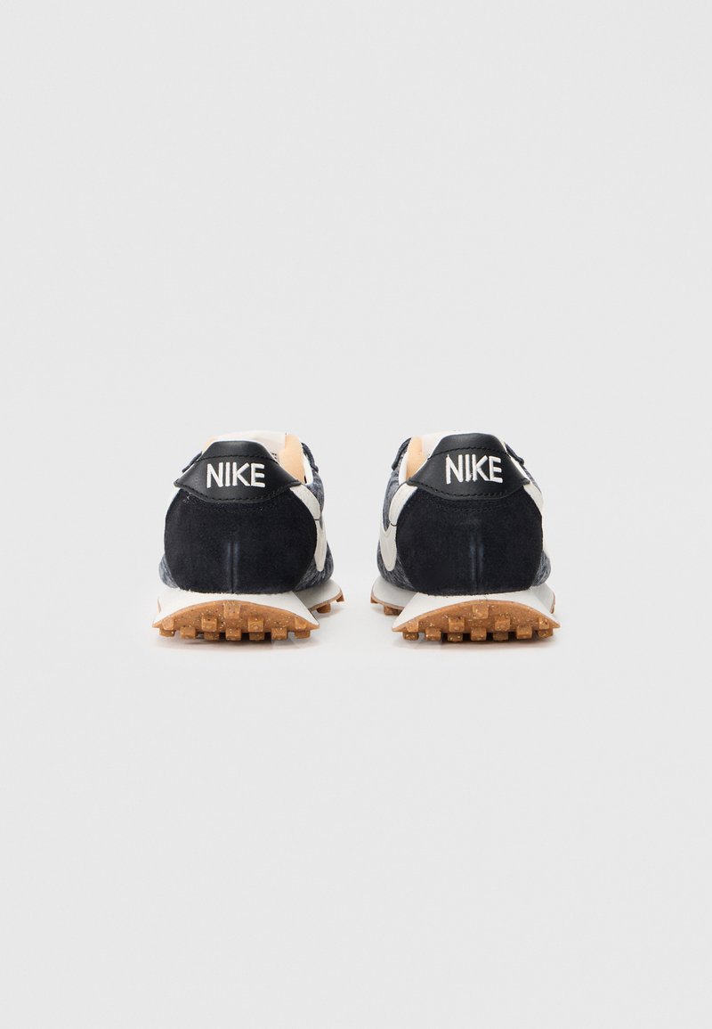 Scarpe da corsa in suede blu navy con dettagli bianchi, dotate di una suola testurizzata e una linguetta sul tallone nera con la scritta "NIKE" in bianco.
