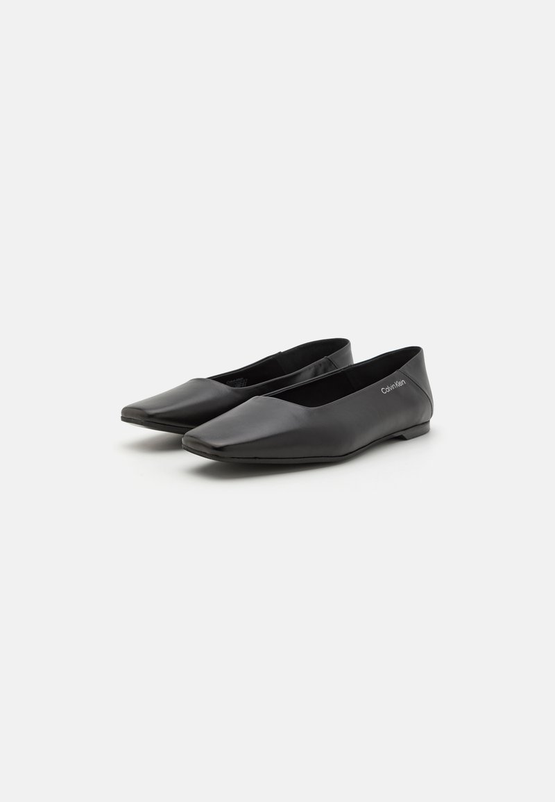 Flats en cuir noir avec un design à bout pointu. Texture lisse, style minimaliste, avec une étiquette de marque sur le côté et une semelle discrète.