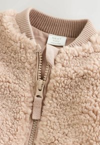 Jachetă bomber din fleece, în nuanță bej deschis, cu guler ribbed, închidere cu fermoar cu accesorii bej și suprafață texturată. Etichetată "NEXT baby."