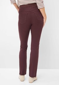 Bordeaux stretchbroek met een soepele textuur, voorzien van twee achterzakken en een hoge taille. Gecombineerd met lichtbeige schoenen.