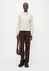 Maglione a coste crema con maniche lunghe, abbinato a pantaloni dritti marrone scuro e a una piccola borsa a tracolla bordeaux. Scarpe con plateau nere.