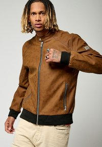 Veste bomber en cuir marron avec fermeture éclair à l'avant, poignets noirs côtelés et texture à motifs sur les épaules ; dispose de deux poches latérales.