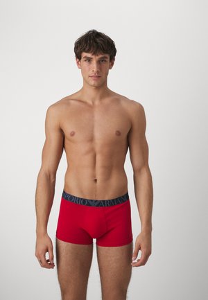 Boxer-briefs rouges avec une ceinture élastique marine arborant le logo "Emporio Armani". Le matériau semble lisse et ajusté.