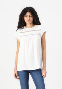 White short-sleeve blouse with lace detailing across the chest and a rounded neckline. Flowy design with textured accents at the sleeves.