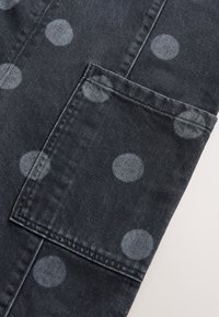 Tissu en denim foncé orné de grands pois gris clair. Comprend une poche plaquée sur le côté avec des détails de couture soignés.
