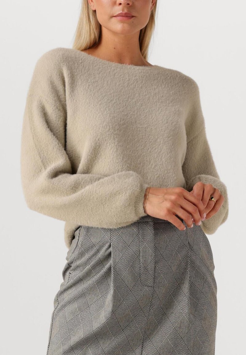 Lichtbeige, zachte fleece trui met een brede halslijn en verlaagde schouders. Gecombineerd met een geruite grijze rok met plooien.