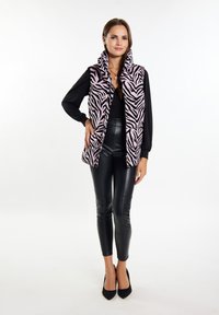 Lyserød zebra mønster puffer vest med høj krave, båret over en sort top, parret med sorte læderleggings og sorte spidse hæle.