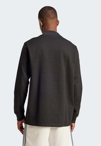 Long-sleeve black sweatshirt with a round neckline, soft fabric texture, and a straight hem. Minimal design with no prominent accents.