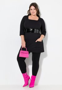 Abito nero con maniche a tre quarti e scollo quadrato, cintura cintrata in vernice nera, abbinato a leggings neri e stivali alla caviglia rosa brillante.
