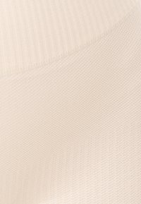 Detailní záběr na krémově zbarvenou látku, která ukazuje dvě pletené textury s diagonálním švem spojujícím žebrované a hladké části.