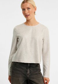 Sølvfarvet langærmet top med tekstureret m�ønster, rund halsudskæring og cropped design, parret med mørke jeans.