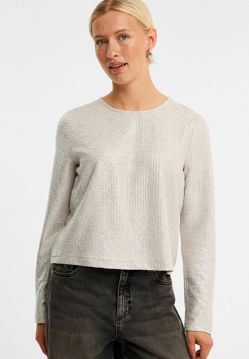 Zilveren top met lange mouwen en een textuurpatroon, ronde halslijn en cropped ontwerp, gecombineerd met donkere jeans.