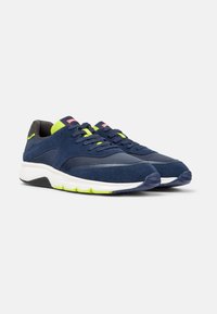 Scarpe sportive blu navy con accenti verde brillante, design con lacci e suola bianca, esposte su uno sfondo semplice.