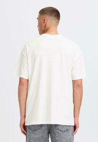 White cotton T-shirt with a relaxed fit and short sleeves, viewed from the back. Basic design with no visible patterns or accents.