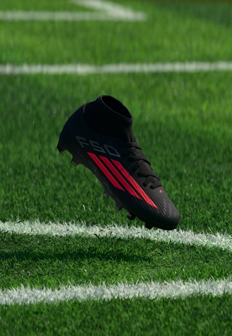 Chaussure de football noire et rouge en l'air au-dessus de l'herbe verte près des lignes blanches sur un terrain de football.