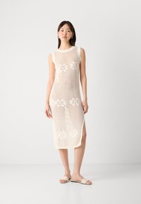 Knit sleeveless dress in beige, featuring floral patterns and a side slit. Textured mesh fabric offers a lightweight appearance.
