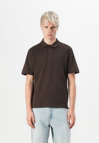 Bruine polo met een zachte katoenen stof, voorzien van een kraag, korte mouwen en een subtiele logodetail op de borst.