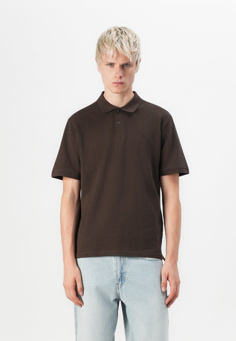 Bruine polo met een zachte katoenen stof, voorzien van een kraag, korte mouwen en een subtiele logodetail op de borst.