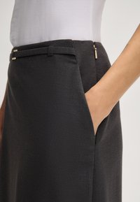 Gonna nera sartoriale con una superficie liscia, tasca laterale e chiusura con zip arricchita da hardware dorato, presenta un design con vita piatta.