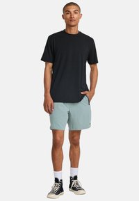 Camiseta negra de manga corta, pantalones cortos verde claro, calcetines tobilleros blancos y zapatillas altas negras. Diseño simple, tejido ligero, corte relajado.