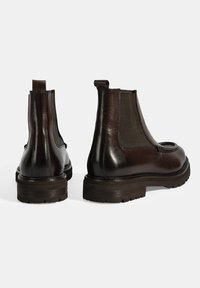 Bottines Chelsea en cuir marron foncé avec des panneaux latéraux en élasthanne, un bout arrondi, une languette et une semelle en caoutchouc texturée. Présente des finitions lisses et mates.