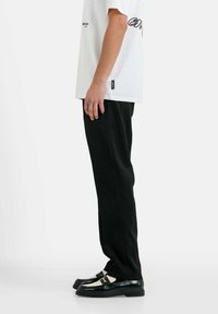 Zwarte broek met een rechte snit, gecombineerd met een witte t-shirt met korte mouwen en zwarte tekst, en zwarte schoenen met witte accenten.