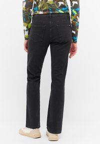Jeans de mezclilla negra con un diseño de pierna recta, que cuentan con dos bolsillos traseros y costuras visibles. Llevados con zapatillas beige.