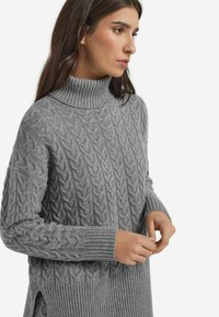 Grauer Kabelstrickpullover mit einem gerippten Rollkragen, langen Ärmeln, seitlichen Schlitzen und strukturierten Mustern. Weicher, warmer Stoff.