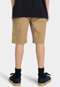 Khaki shorts van katoen, met een ontspannen pasvorm, afgewerkte randen, en gecombineerd met donkerblauwe suède schoenen en zwarte enkelsokken.